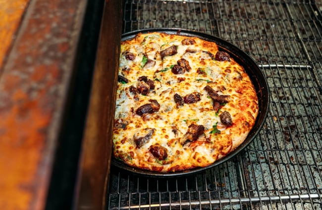 A meat and cheese pizza coming out of a pizza oven.