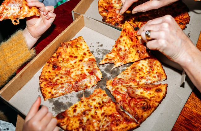 Hands holding slices of pizza in a box.