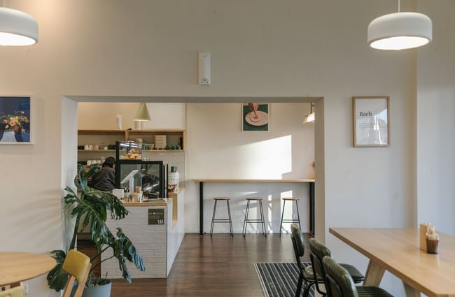 Interior of NOKI in Christchurch with wooden furnishings, green leather chairs, white-tiled countertop and framed art prints including someone sticking their finger in a fried egg