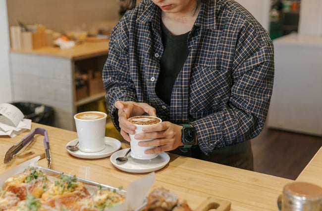 Barista making two coffees in white mugs and placing them on cafe countertop