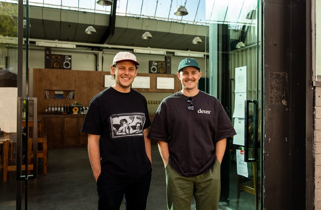 Two men standing in front of their bar smiling at camera.