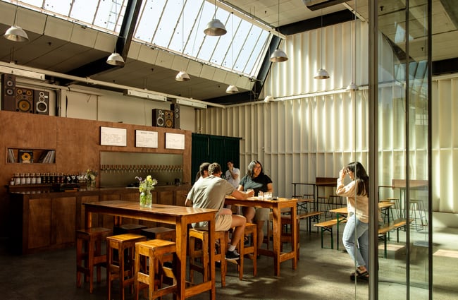 A group of diners sitting at a high table in a brightly lit warehouse-style bar.
