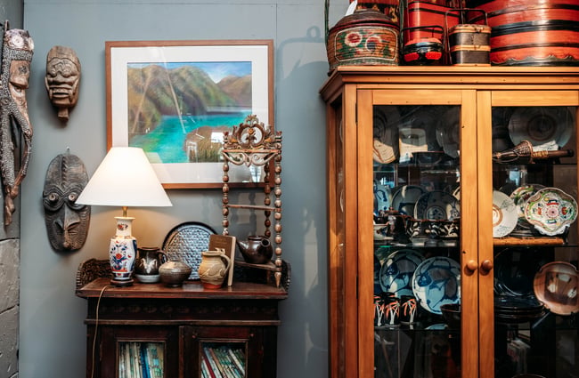 Close up of cabinet filled with china plates next to a wall of art and face sculptures