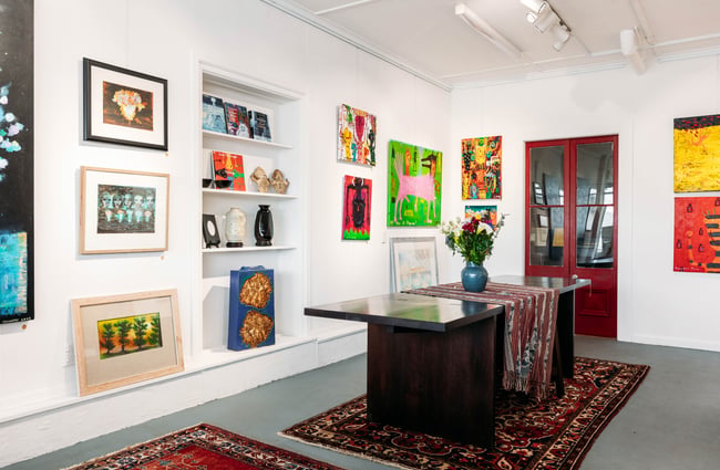 Exhibition space at Oásis in Ōamaru with colourful art on the wall and sculptures and books on shelves