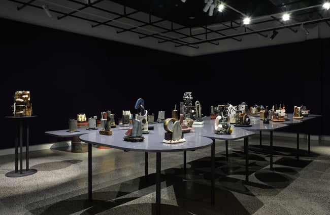 Works of art on display on tables inside a darkly lit gallery.