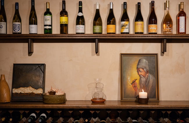 Lineup of wine bottles on a shelf and artwork below at Odeon.