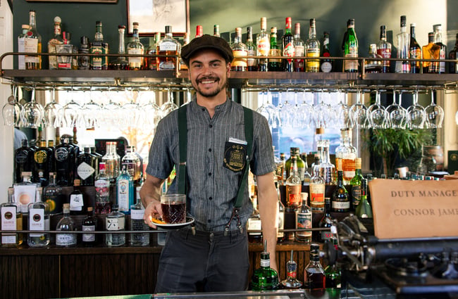 Bartender at OGB smiling behind bar and holding out a glass of mulled wine