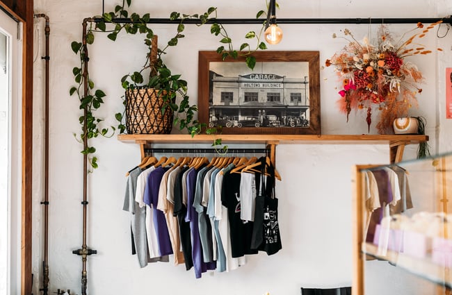 T-shirts for sale hanging from a wooden shelf.