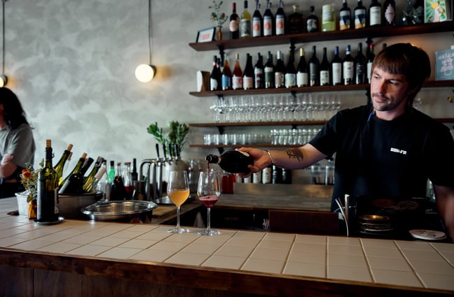 Waiter pouring two glasses of wine on bar top at OOH-FA in Auckland
