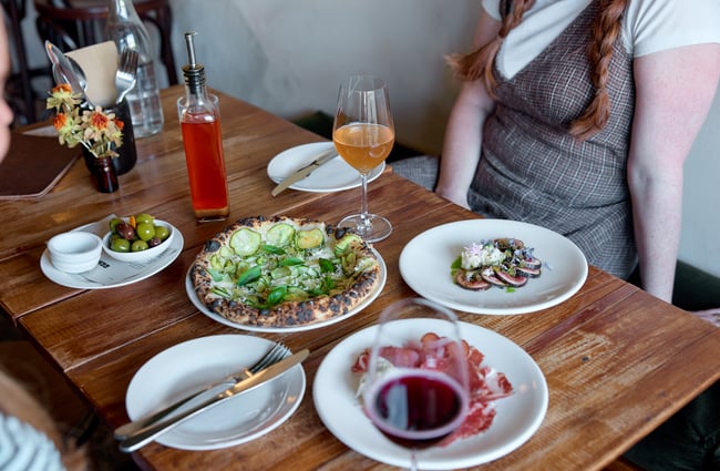 Pizza and a selection of dishes and wine on table at OOH-FA in Auckland