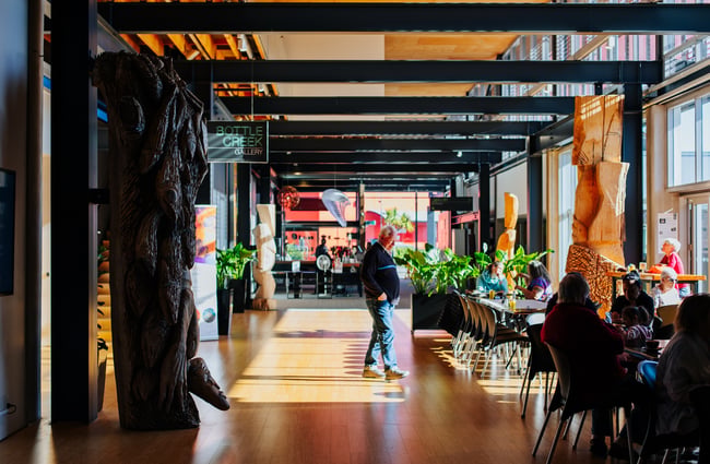 Looking down a wide, sunny corridor at Pātaka with tables and chairs along the window side.