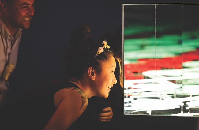 A woman looks closely at artwork in a dark room at Pātaka.