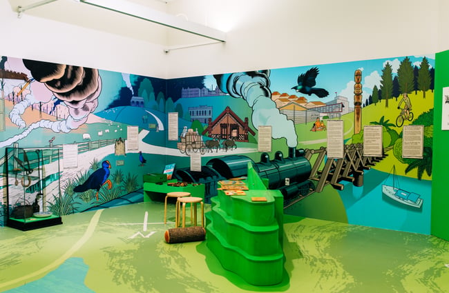The kids' zone at Pātaka with a mural wrapping around the walls and interactive games in the middle of the green space.