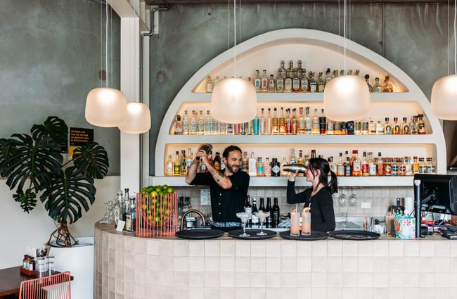 Two bartenders are behind the bar shaking cocktail shakers at Paloma.