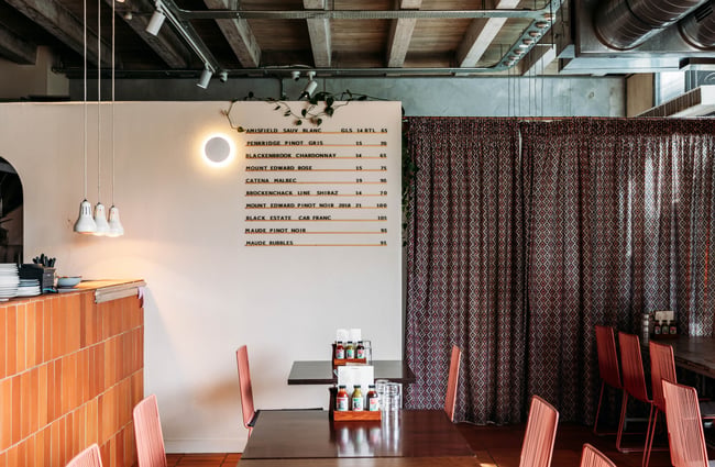 An interior image looking across past the kitchen to the white wall with a drinks menu displayed.