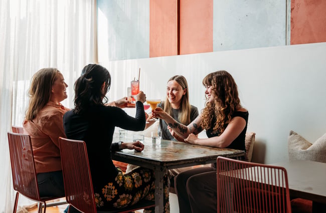 A table of customers are holding up their drinks doing a cheers at Paloma.