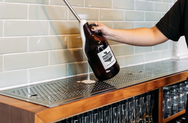 Someone holding a takeaway rigger of beer under tap with foam coming out of the top