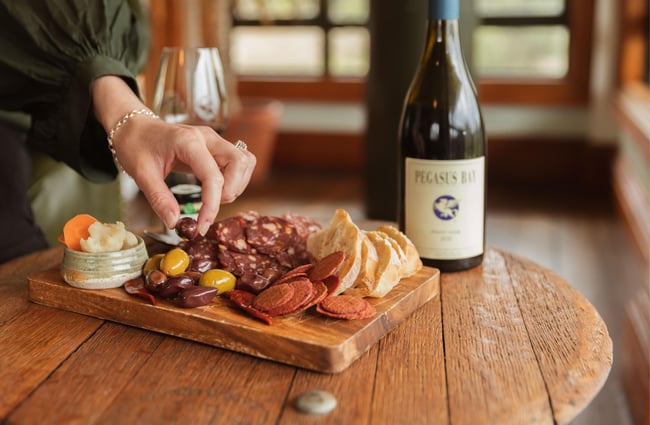 A hand reaching for an olive on a cheese board.