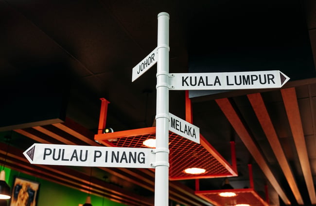 Geographical signage pointing to destinations in Malaysia in Penang Street Food.
