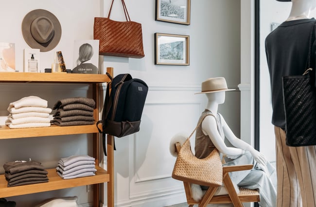 Folded knitwear on wooden shelves and mannequins accessorised with hats and woven shoulder bags.