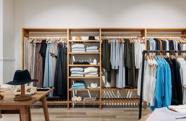 Clothes hanging on racks and hats on shelves within a freestanding wooden structure.