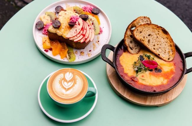 A cup of coffee and plates of breakfast on a green table.