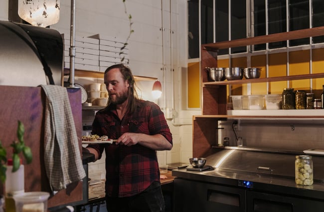 Man putting pizza into woodfire oven.