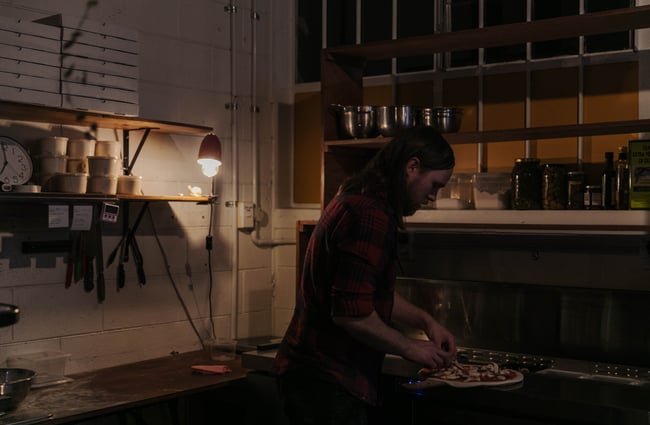 Man putting toppings on a pizza.