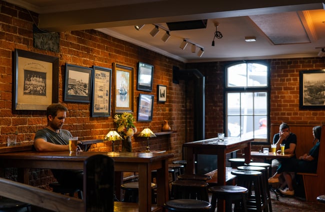 The dimly lit interior of Pomeroy's with dark wooden high tables and framed photographs hung on the brick walls.