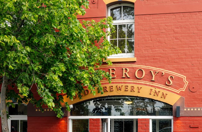 Close up of the signage above the front door of Pomeroy's, partially obscured by a tall, leafy green tree.