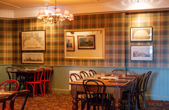 A dining area inside Pomeroy's where the tables are laid for service. The floor is retro patterned carpet and the walls are wainscoted, painted a pale blue, with plaid wallpaper above.