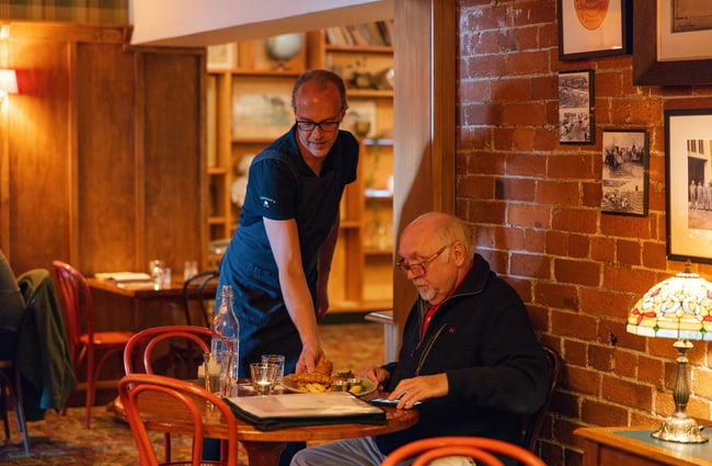 A server places a plate of fish and chips in front of a customer seated at a small round table inside.