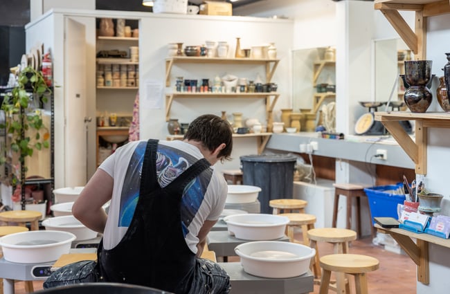 Potter at work with shelves of products in the background at Pottery Capital.