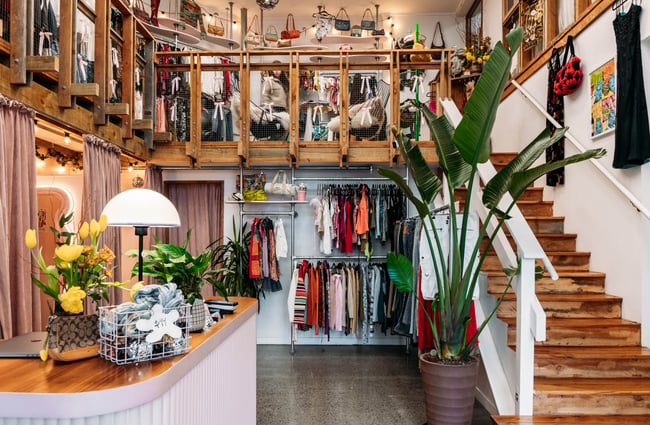 Front counter, clothing racks and stairs leading up to more clothing at Preloved Charlies.