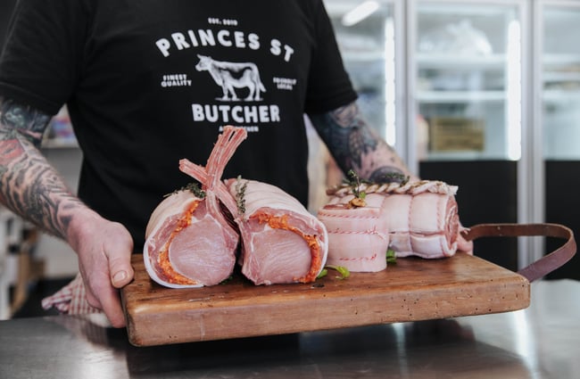 A person holding a chopping board of raw meat cuts.