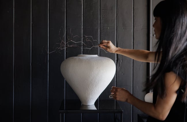 A branch being placed onto a white vase.