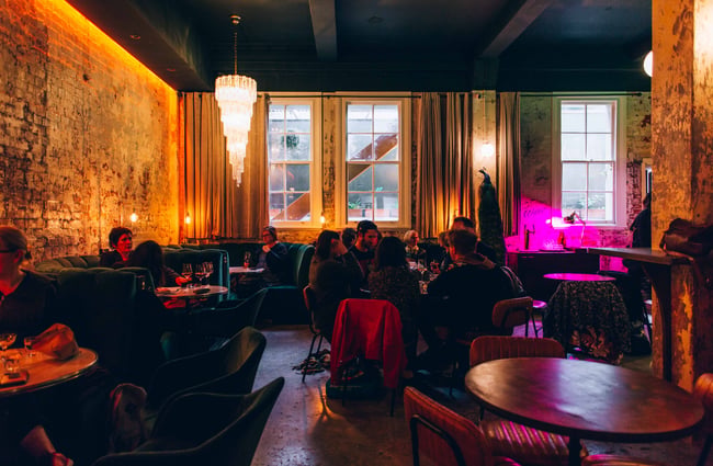 People seated in a dimly lit restaurant with tables and booth seating.