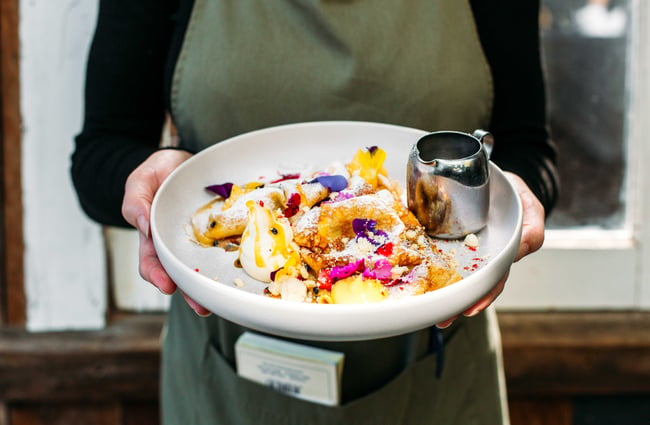 A staff member holding a colourful plate of crepes.
