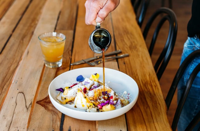 Maple syrup being poured onto a plate of crepes on a wooden table.