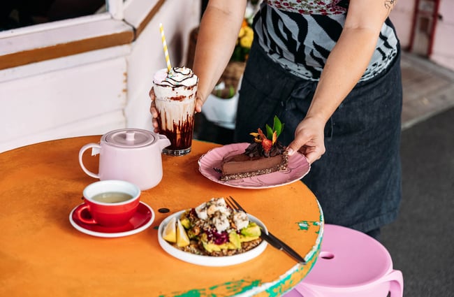 Someone placing plate of cake on table next to drink and salad