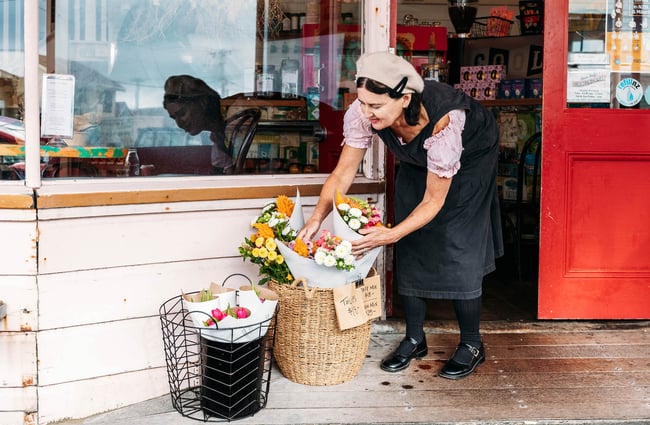 Woman placing flower bouquet outside door of Queen Sally's Diamond Deli in Lyall Bay Wellington