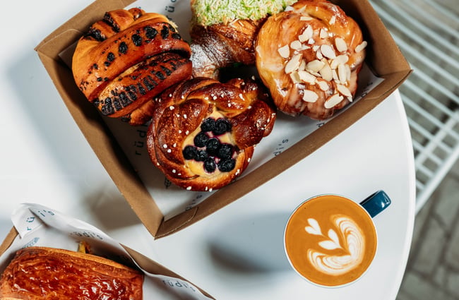 A cup of coffee sits on the table with a selection of pastries.