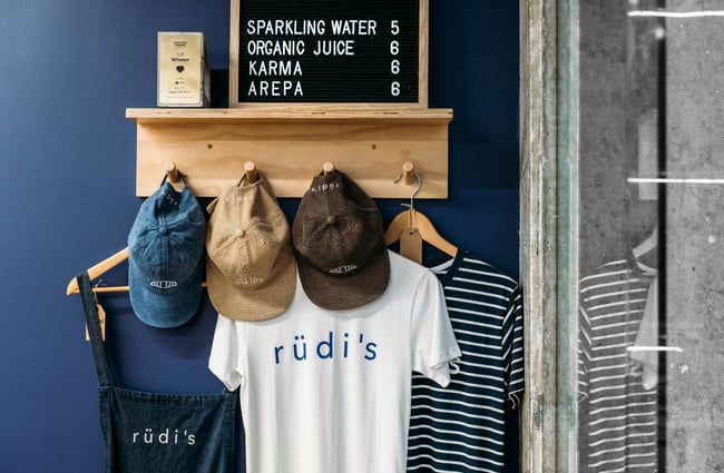A selection of merchandise including t-shirts and caps are on display on a rack on a wall.