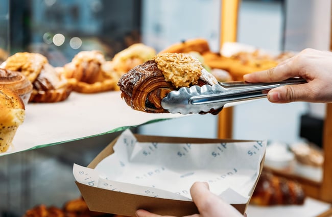 A shop assistant selects a pastry from the cabinet.