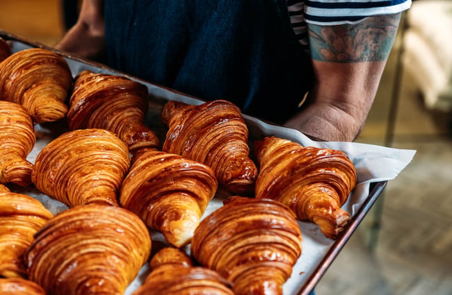 A shop assistant is holding a tray of croissants.