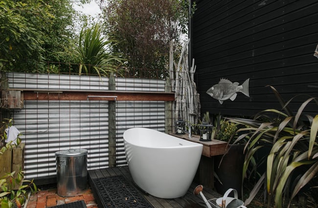 An outdoor bathtub on a black desk surrounded with trees.