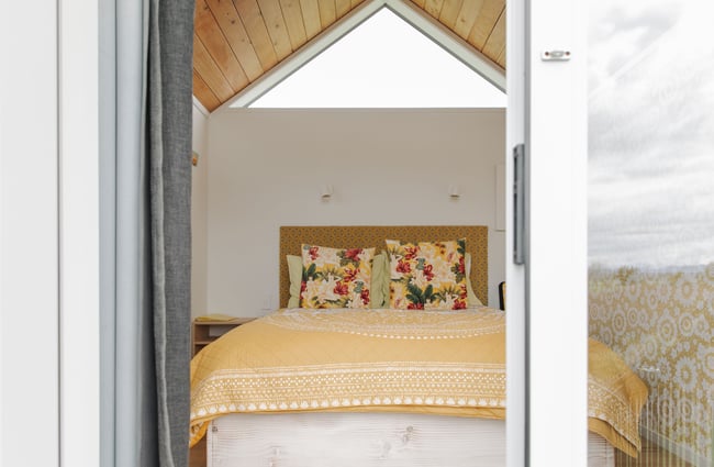 Looking through open glass doors where there is yellow bedding on a queen bed.