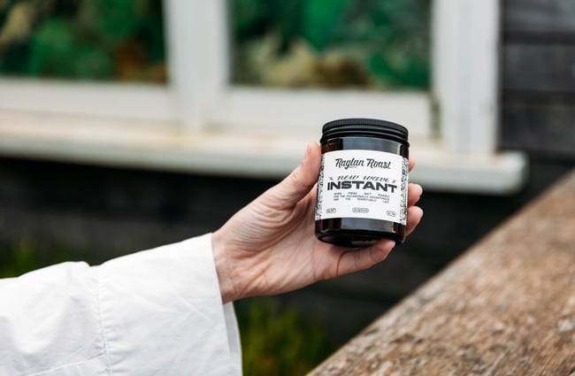 A hand holding a small jar of instant coffee.