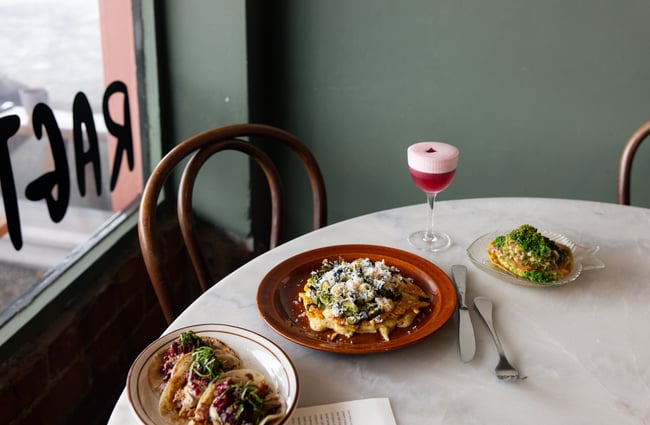A table setting with a pink cocktail and plates of food.