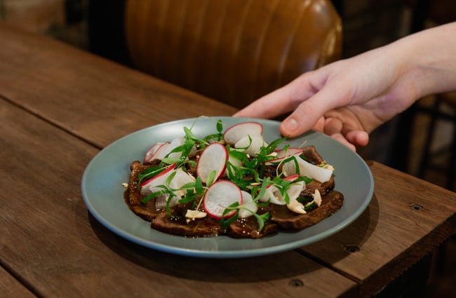A hand holding a plate of food on a wooden table.